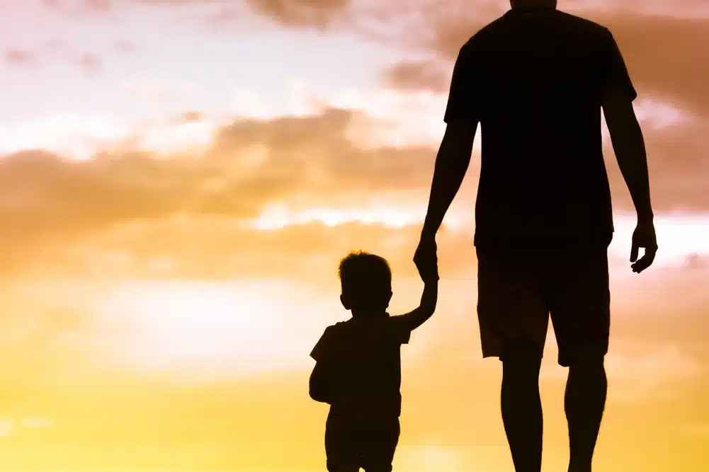 Silhouette of father walking together with little son holding hands facing sunset