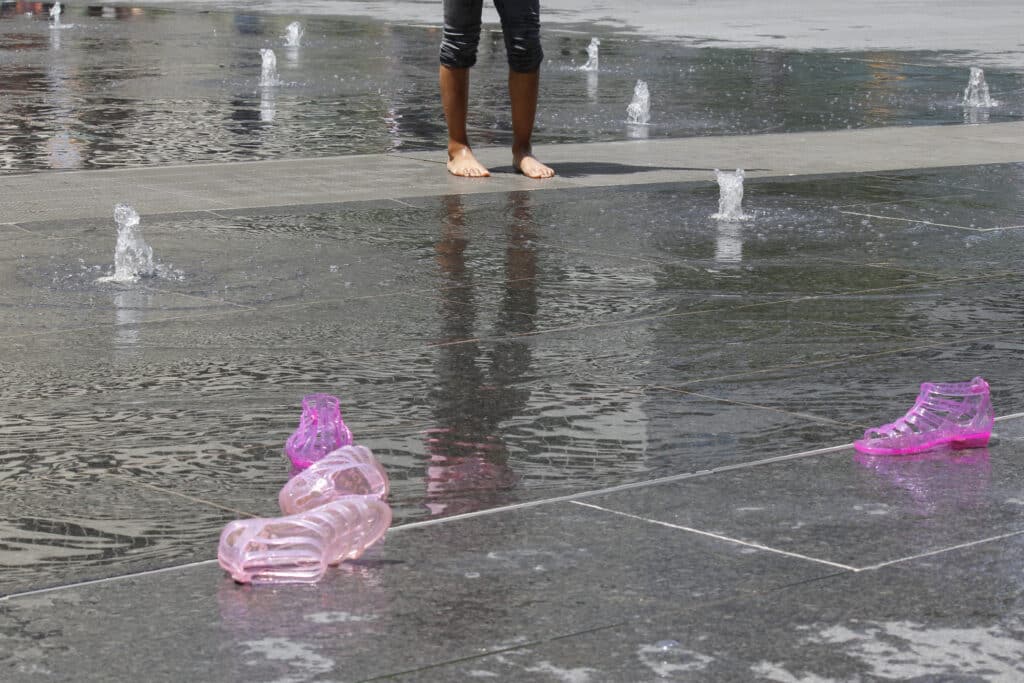 A girl goes barefoot as pink jelly shoes lay discarded by the fountain sprayground in Dilworth Park