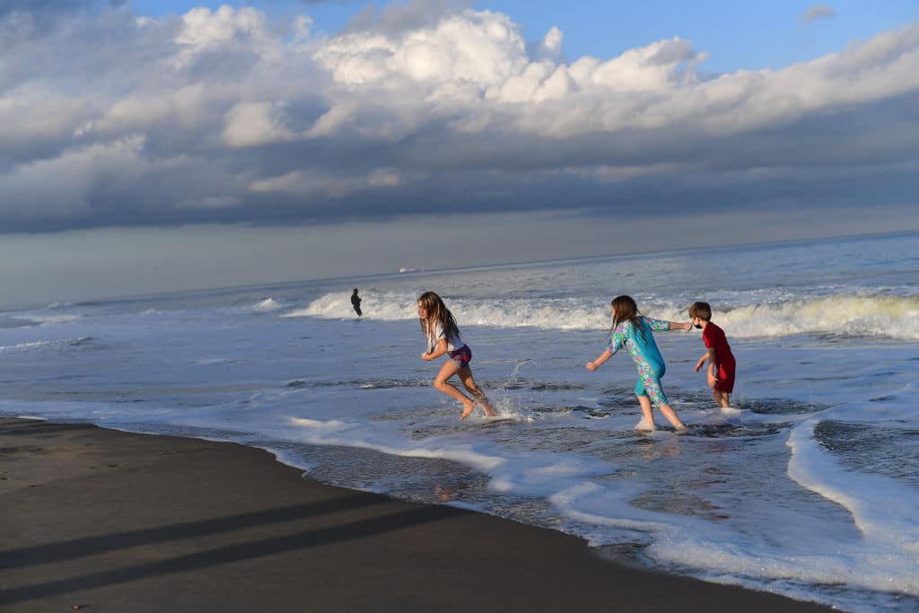 Cicely Somers, 8, Rheya Long, 6, and Hal Somers, 6, play in the ocean surf on Thanksgiving during an unseasonably warm 70 degree day on November 26, 2020 in Rehoboth Beach, Delaware.