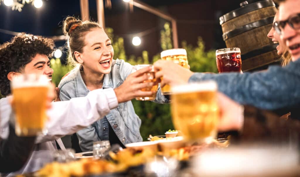 Happy friends clinking and toasting beer at brewery restaurant patio - Life style and beverage concept with young people having fun together out side at patio garden by night - Warm evening filter- Eagleview