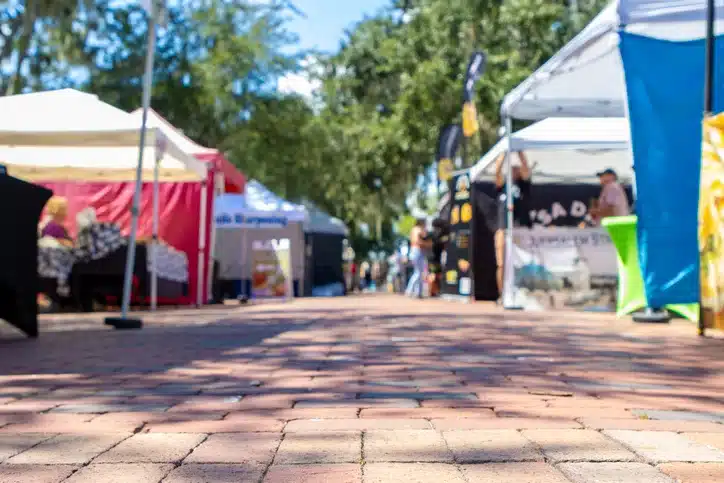 Background photo of vendor tents in an outdoor town festival or farmer's market with a brick sidewalk in the middle.