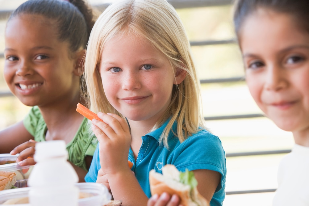 Kindergarten children eating lunch outdoors smiling at camera