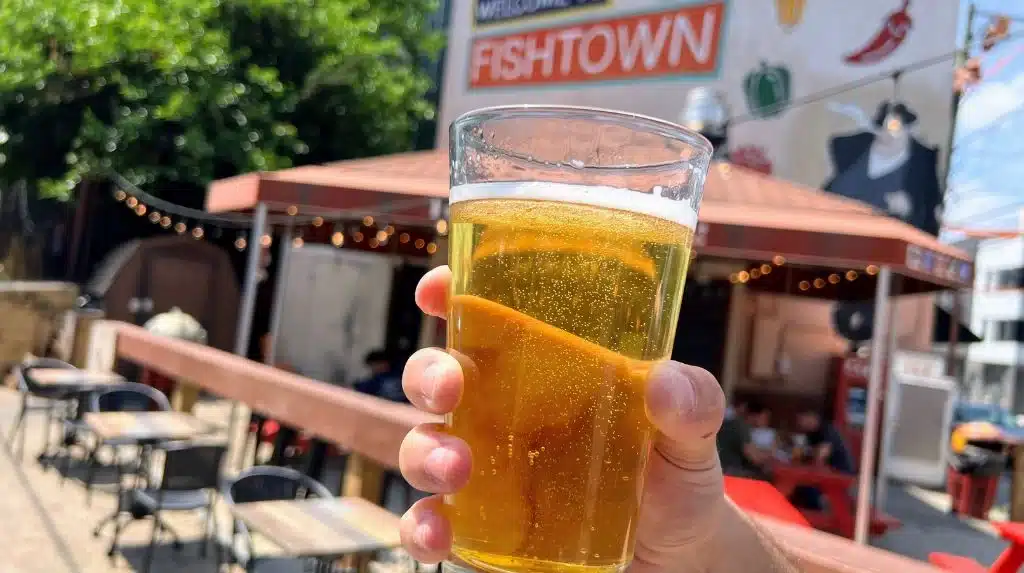 person holding beer in front of welcome to fish town mural for fishtown taps