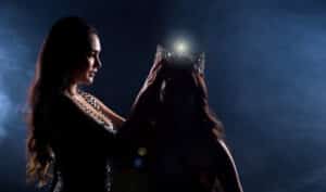 Two Miss Asian Women Pageant Beauty Contest in Evening Ball Gown dress wearing silver diamond crown on head sash, waiting final announcement moment, dark smoke background low key exposure silhouette