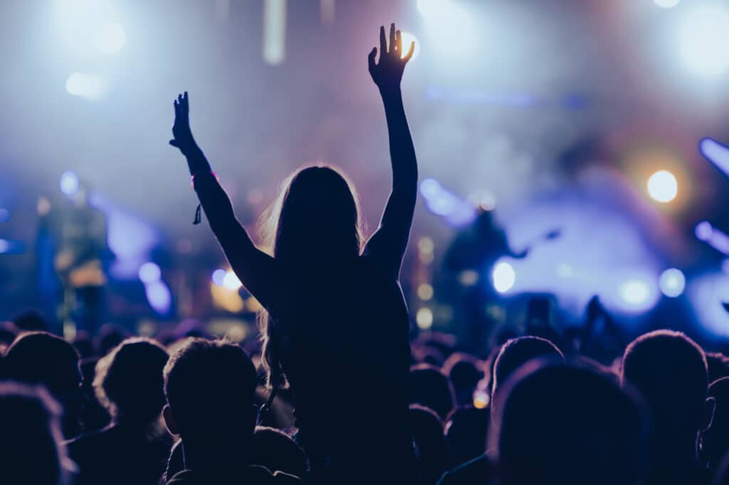 Silhouette of a woman in a crowd watching concert at open air music festival and enjoying. Crowd with raised hands.