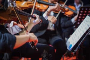 Hands playing violin orchestra with note sheet on stage.